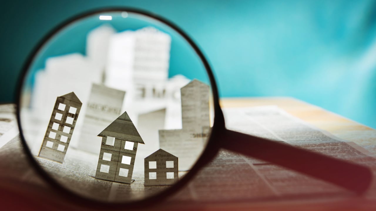 Paper house cutouts under a magnifying glass on printed financial pages.