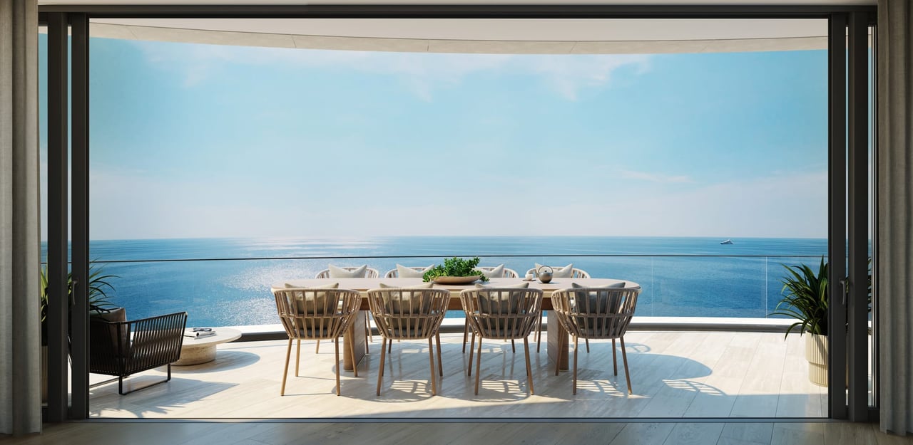 Oceanfront terrace with a dining table and woven chairs overlooking the water.