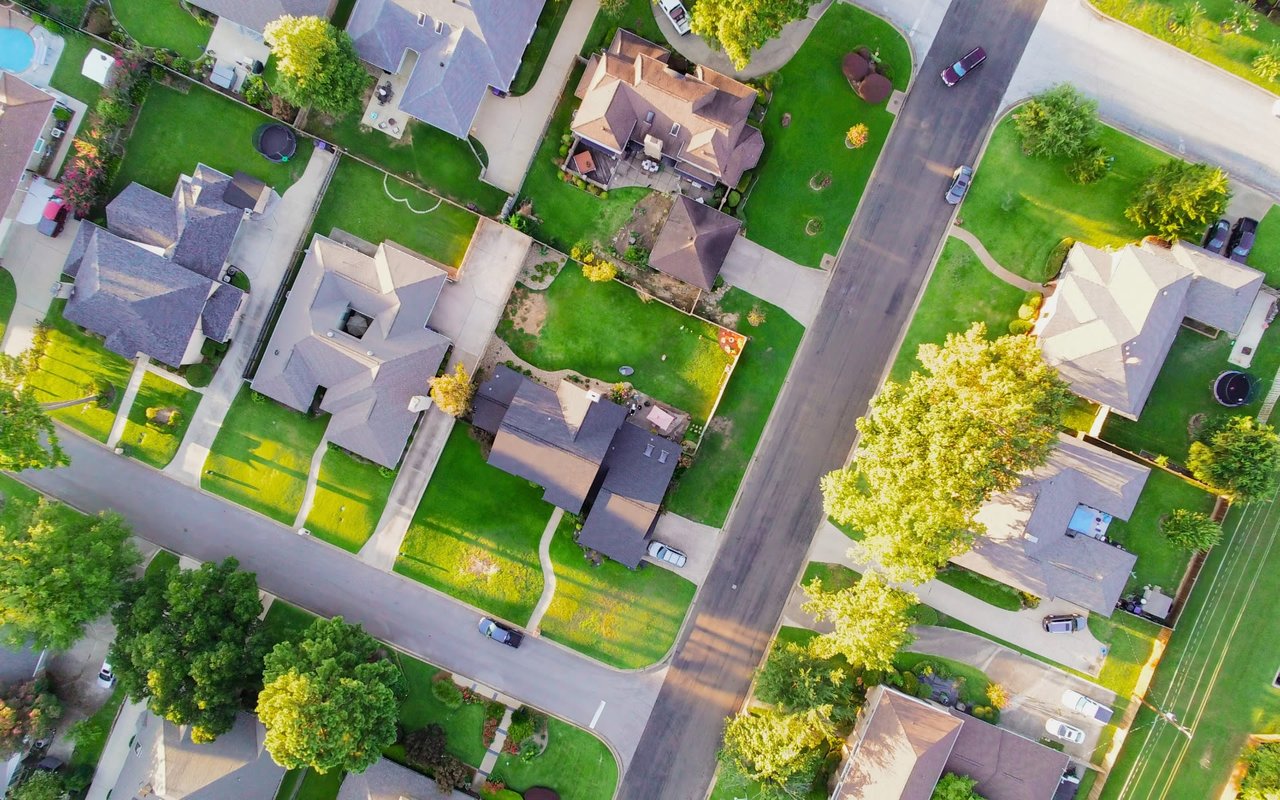 Aerial view of a quiet neighborhood with curving roads, houses with yards, and many trees.