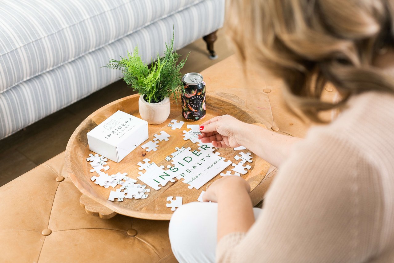 A real estate agent from Insiders Realty is piecing together a puzzle on a wooden coffee table.
