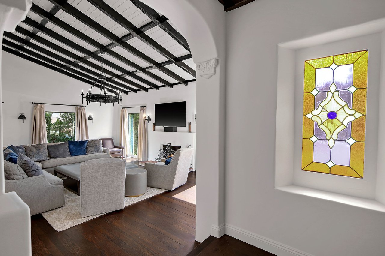 An ornate stained glass window, featuring a symmetrical design in yellow, purple, and clear glass with a blue central accent, is set into a thick white wall on the right side of the image.