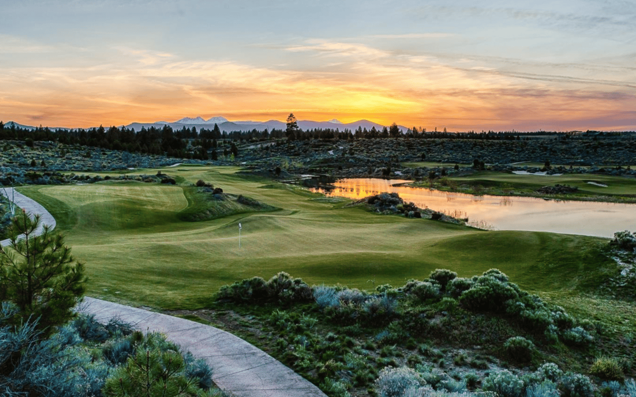 a beautiful view of a green plain golf course overlooking the mountain ranges