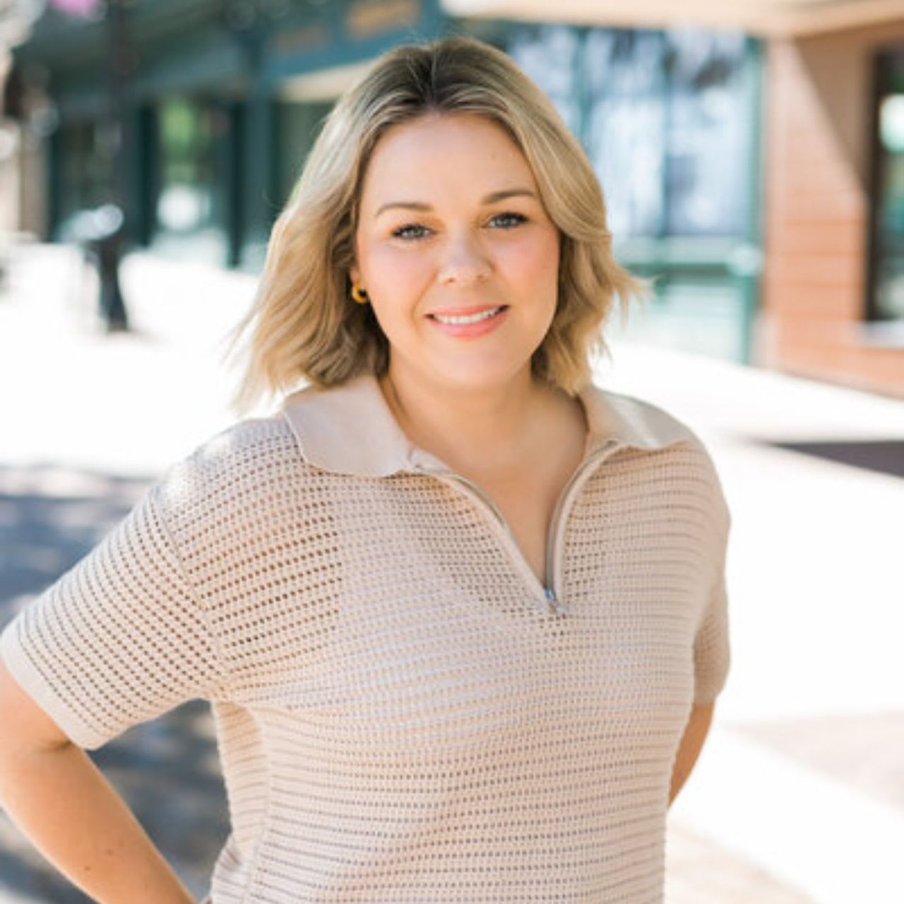 Cait Berry, a real estate agent from the Insiders Realty team, is standing on a sidewalk wearing a beige sweater.