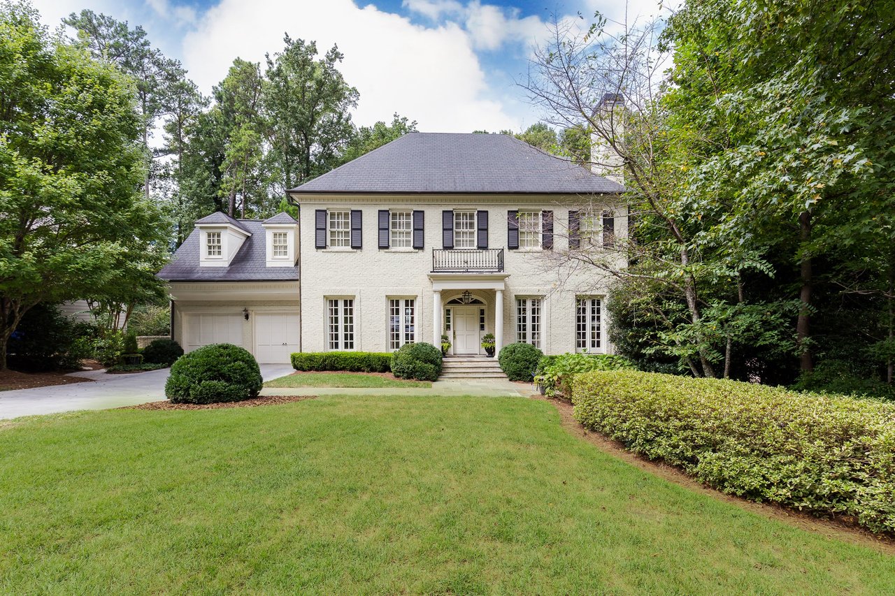 Two-story white house with a black shingled roof, green lawn, covered porch, and a two-car garage on the left.