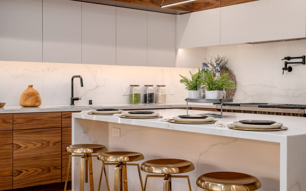 Modern kitchen with a marble island, walnut cabinets, and brass bar stools.