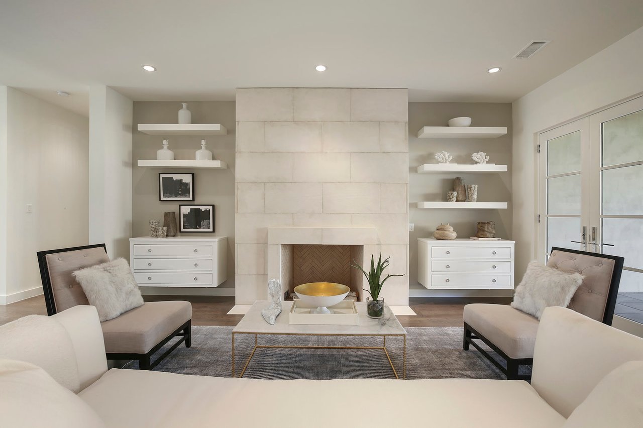 A contemporary living room with a sleek fireplace, white walls, white sofa, and wooden floors.