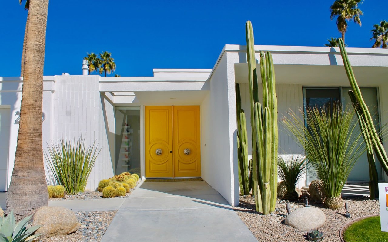 A white house with a bright yellow door and cactus in front of it