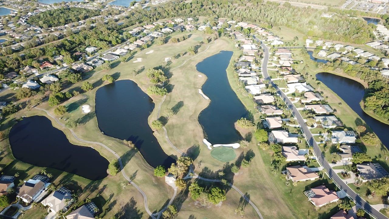 An aerial view of a residential golf course bordered by single-family homes, townhouses, fairways, and greeneries.