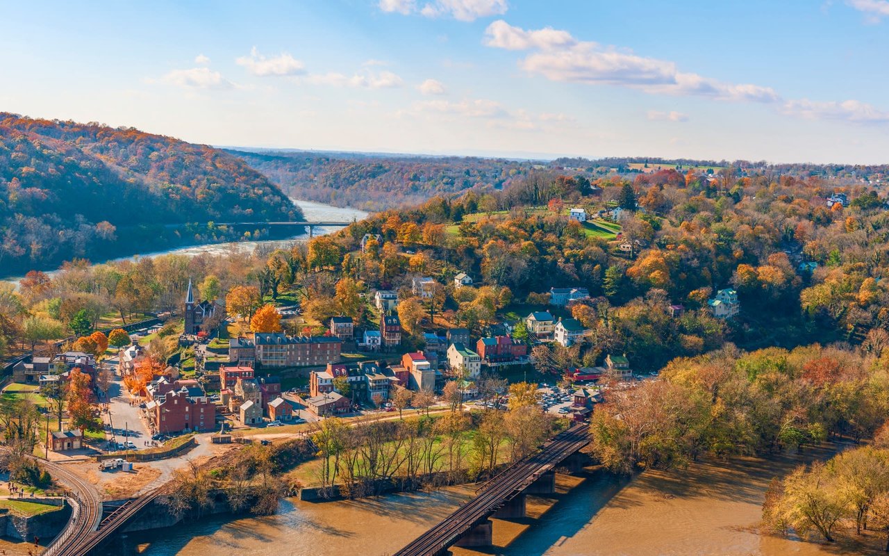  An aerial view of a picturesque town nestled in a valley, surrounded by rolling hills covered in trees displaying vibrant autumn colors.