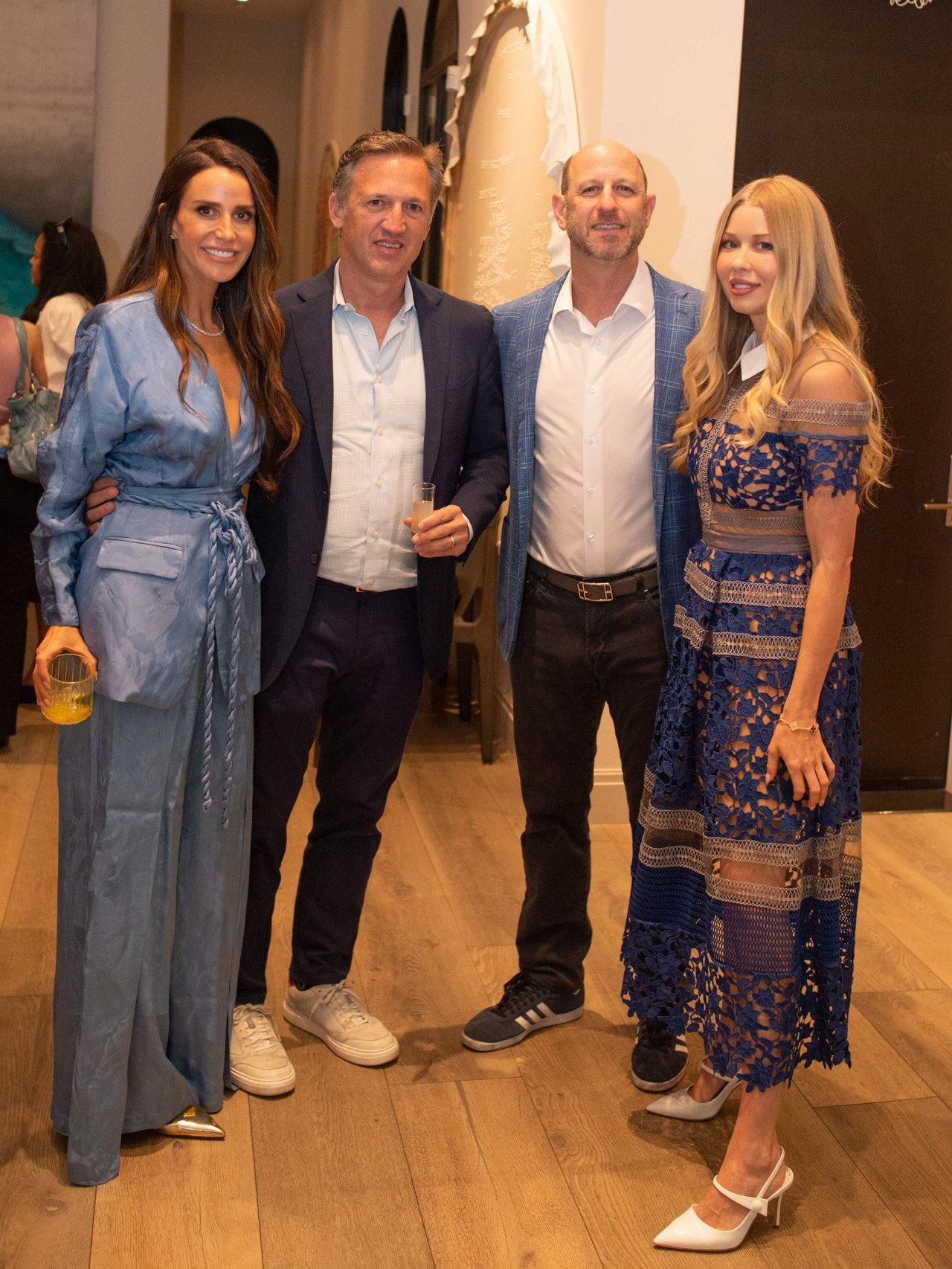 Four adults pose together at an event, including a woman in a blue suit and another in a blue lace dress.