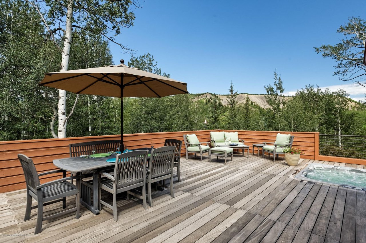 Furnished wooden deck with dining and lounge areas, a hot tub, and wooded ridge views.