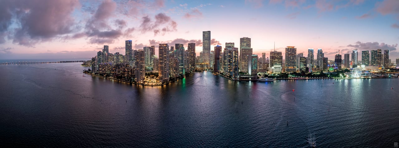 Miami skyline at dusk across the bay, with illuminated waterfront high-rises.