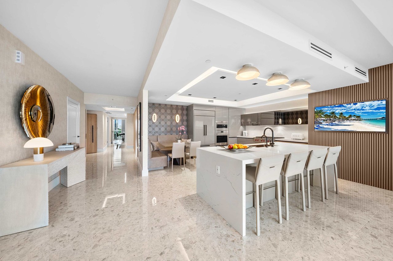 Minimalist kitchen with gray cabinets, large fridge, mirrored backsplash, wood accent wall, and bar area with flat-screen TV.