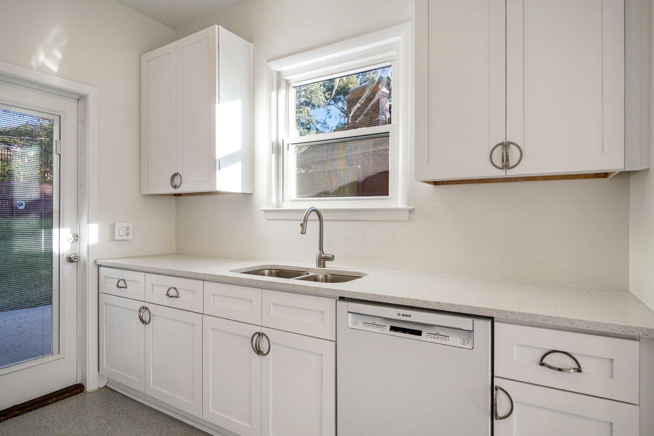 Another view of the kitchen, highlighting the dishwasher, sink, and additional cabinets. The kitchen has a clean, modern look with white fixtures and ample counter space.