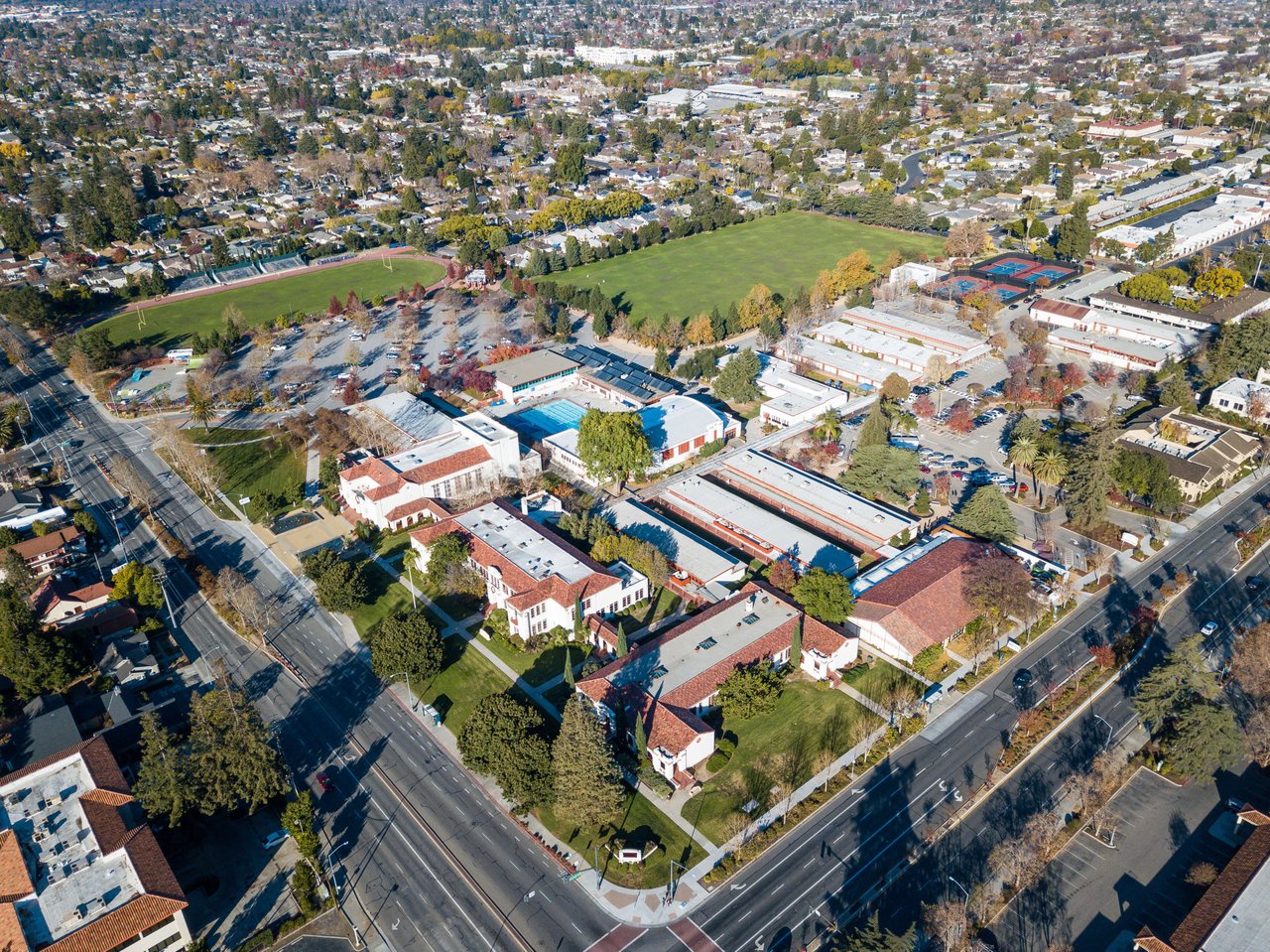 Aerial view of a residential neighborhood with curvy roads, houses with pools, and green backyards.