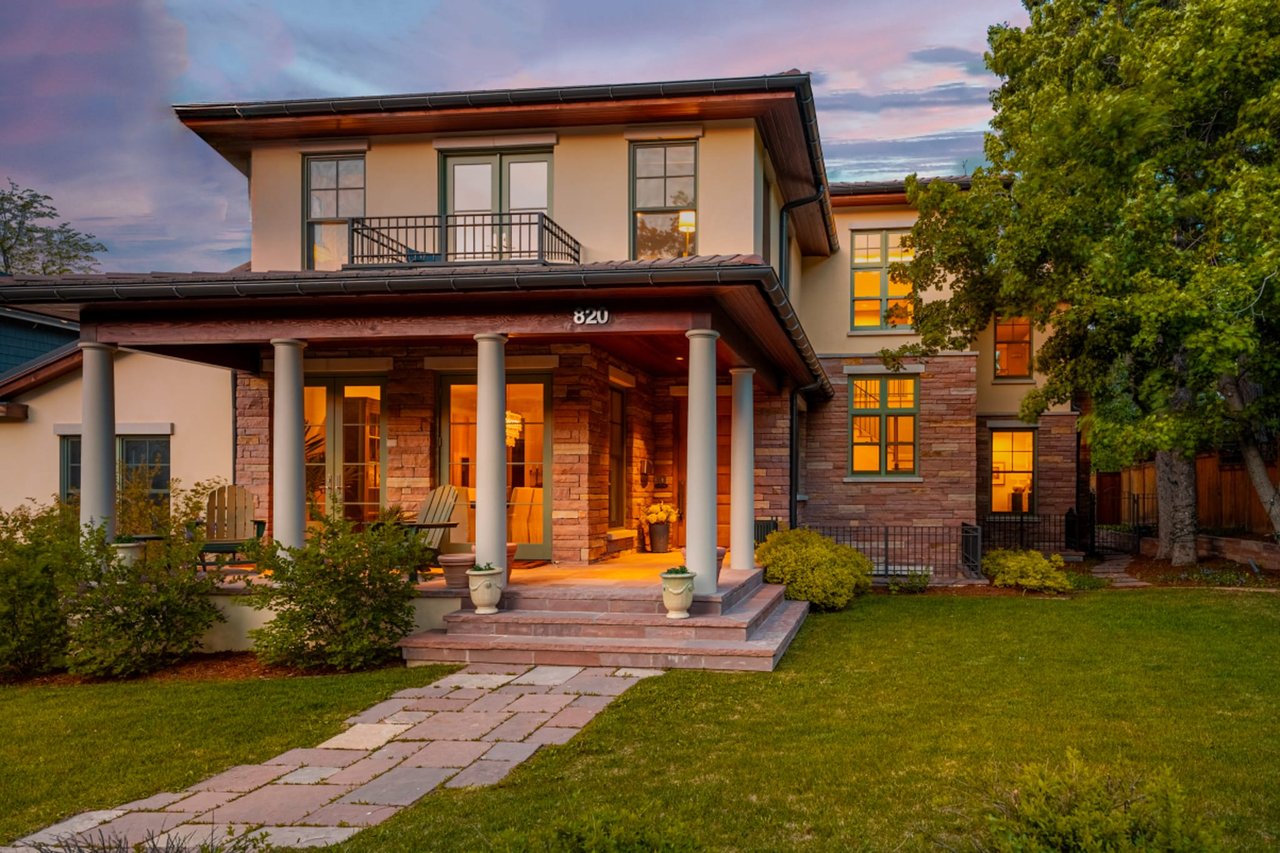 Craftsman home exterior at dusk with stone columns, white trim, and warm interior lighting glowing through windows