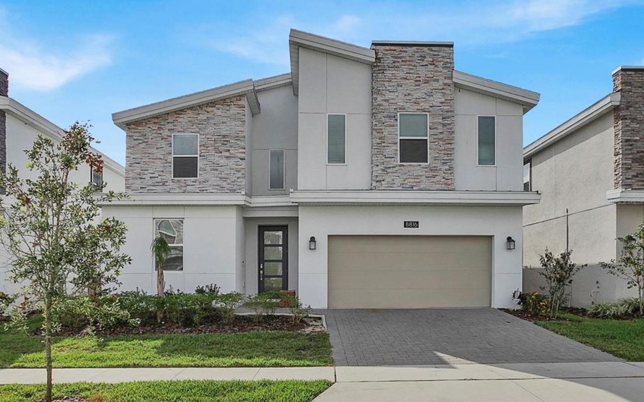 A spacious, white house with a long driveway that leads to a garage, a walkway, and a front lawn.