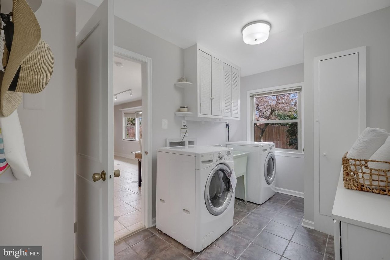 Laundry room with two front-loading machines, a utility sink, and white cabinets.