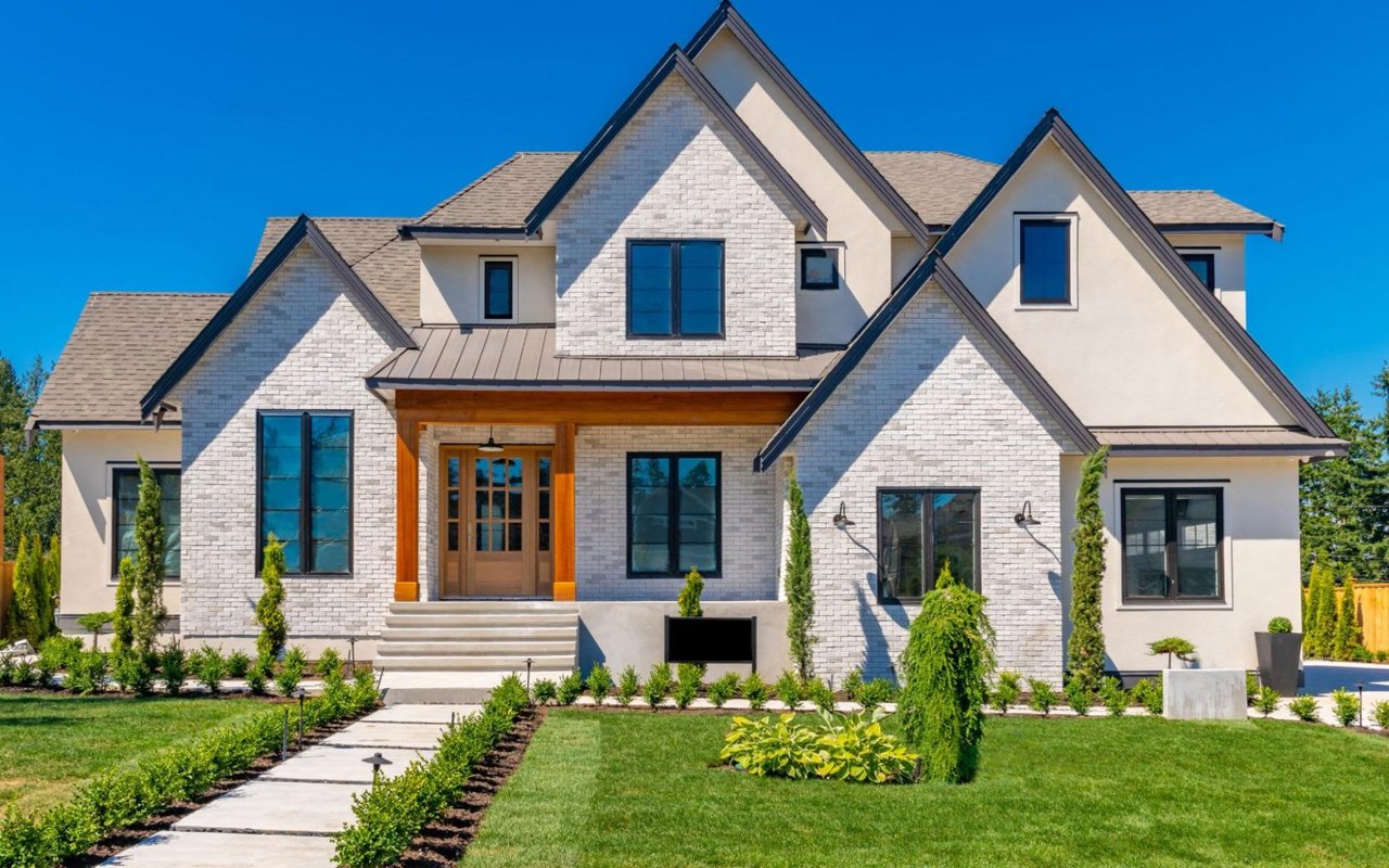 A large white brick house with a lush green lawn in front of it.