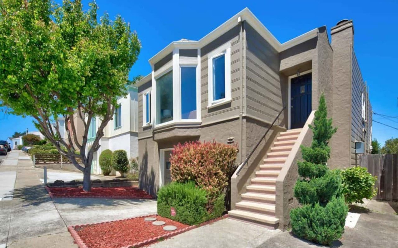 Modern gray home with an elevated dark blue front door, exterior stairs, and landscaped front yard.
