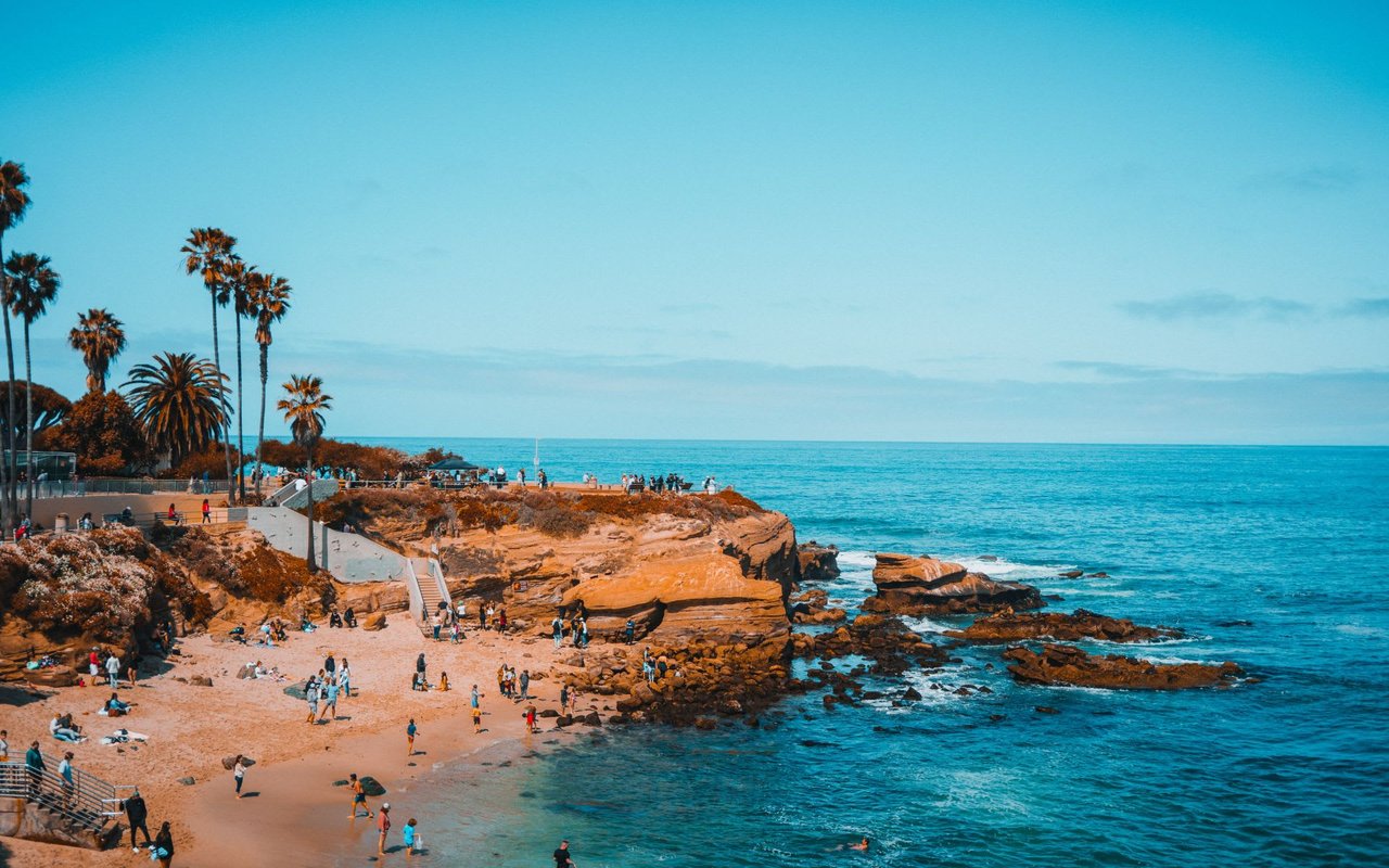 San Diego beach scene with people in the water and standing on the rocks overlooking the surf