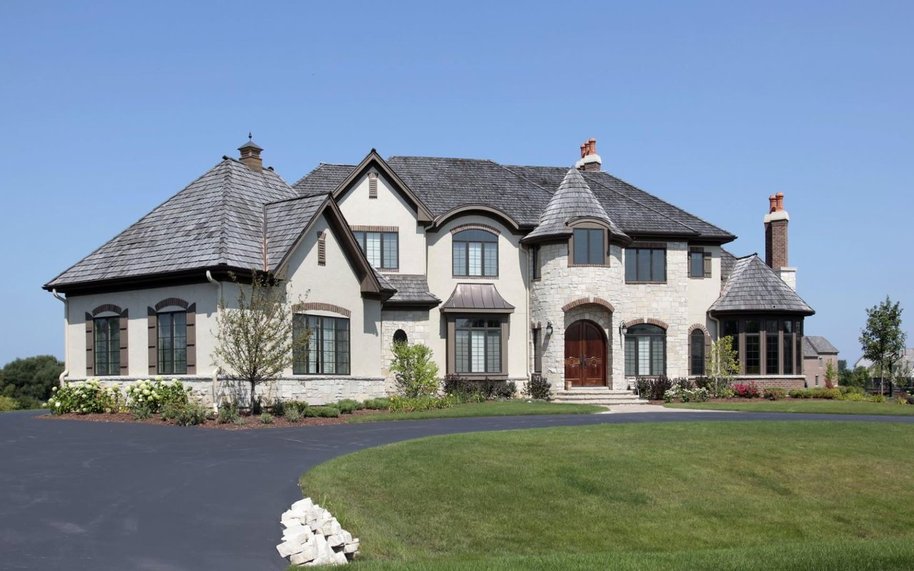 A large white house with a gray roof, many windows, and a long driveway.