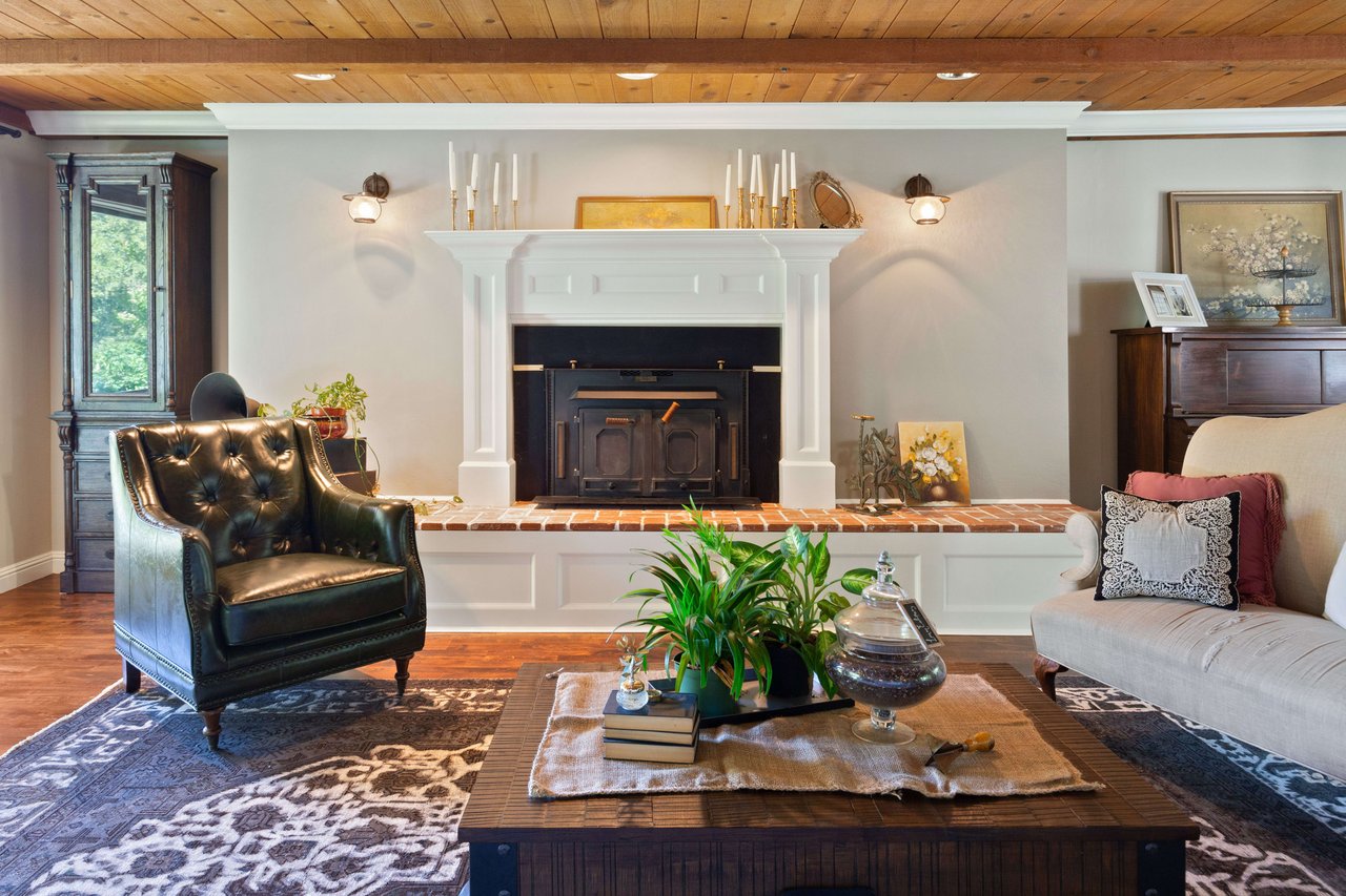 Living room with a white fireplace, wood-plank ceiling, black leather armchair, and patterned rugs.