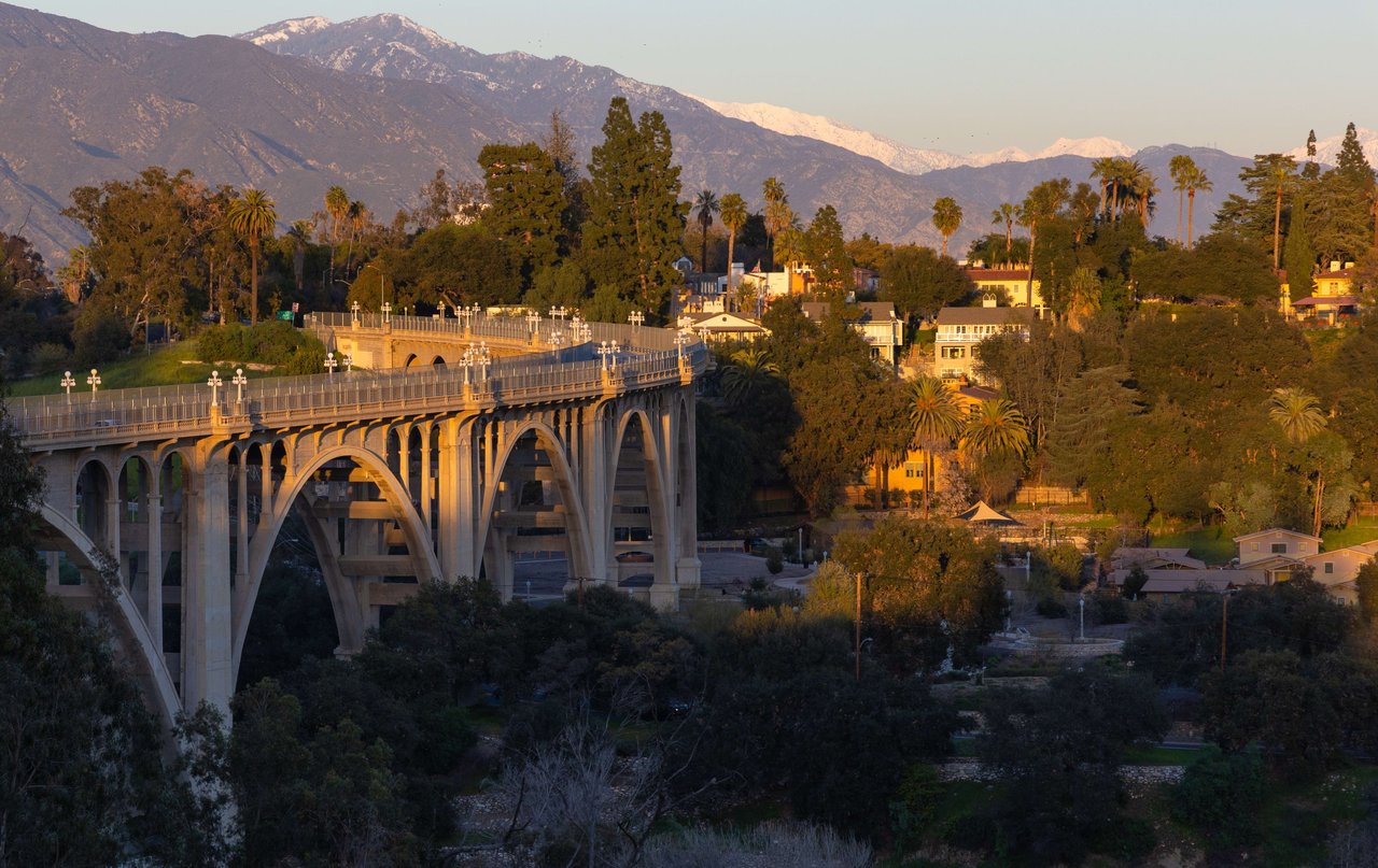 A curved, concrete bridge spanning a road with snow-capped mountains in the background.