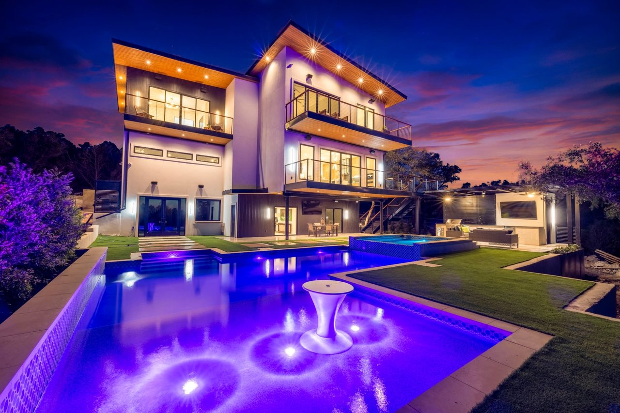 A large house with a swimming pool in front of it at night.