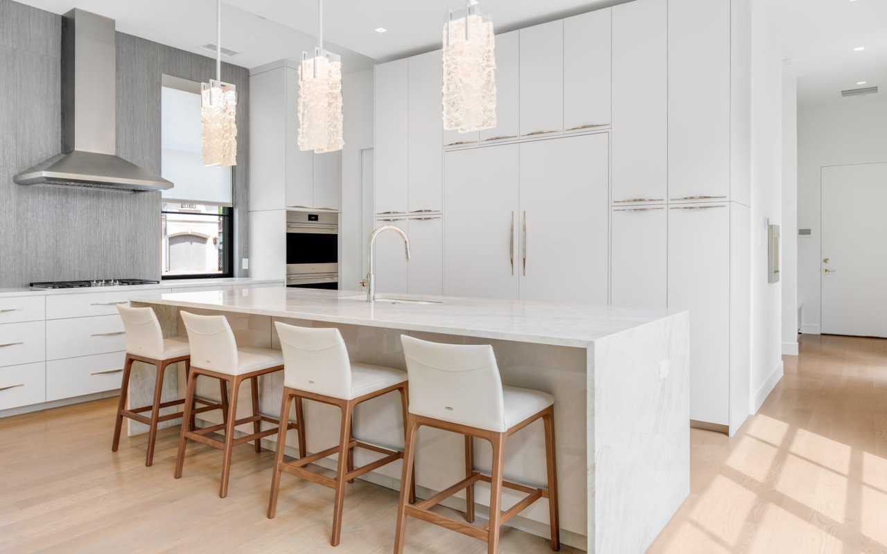 Elegant modern kitchen with white cabinets, countertops, and stools, complemented by stunning, luxurious glass chandeliers.