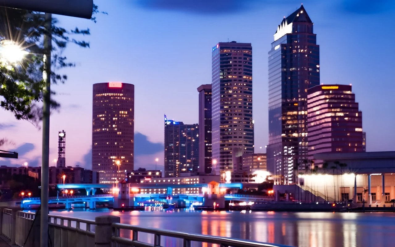 A bridge over a body of water is brightly lit with blue lights, with reflections shimmering on the water's surface. 