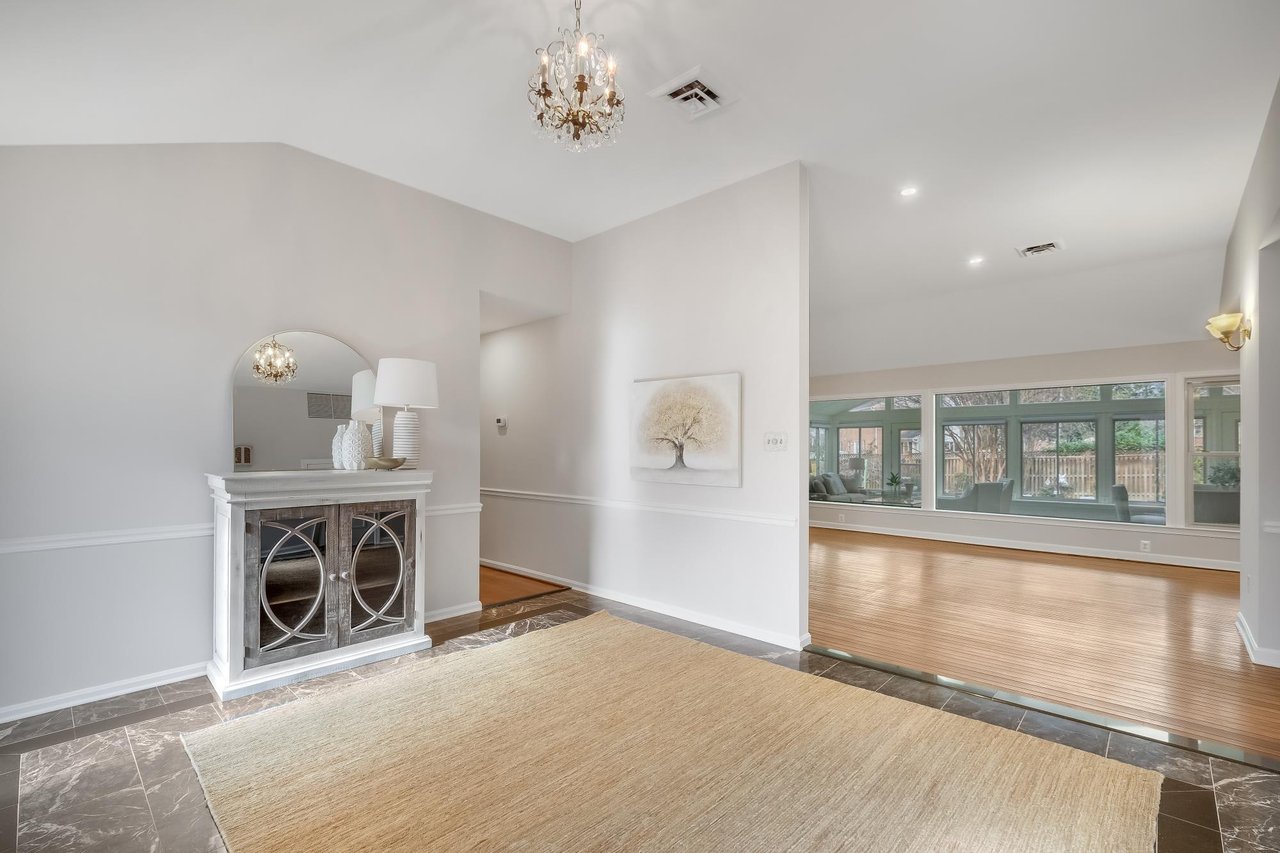 Tiled foyer with a chandelier and decorative console opening to a sunlit hardwood sitting area.