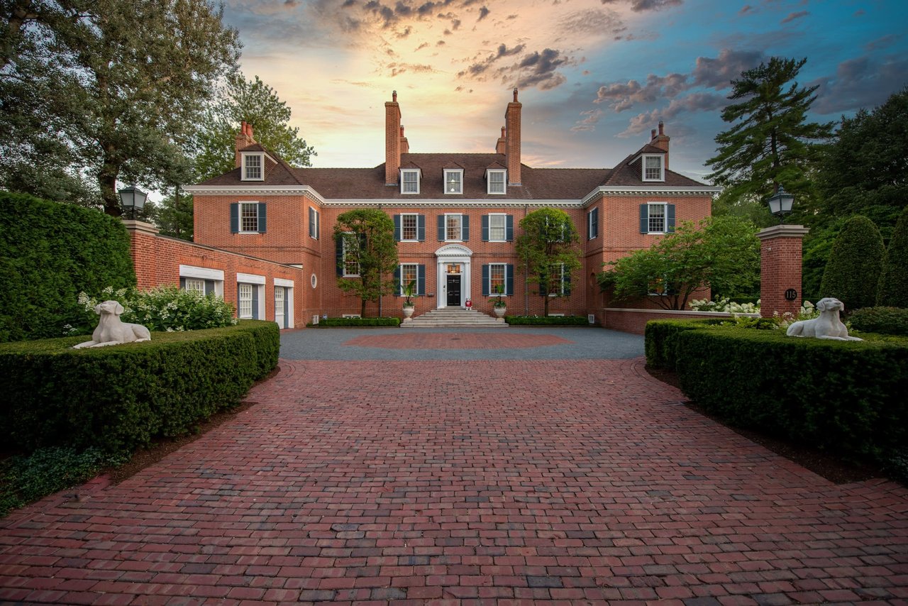 Image of a brick driveway leading to a large house with two statues of dogs in front of it