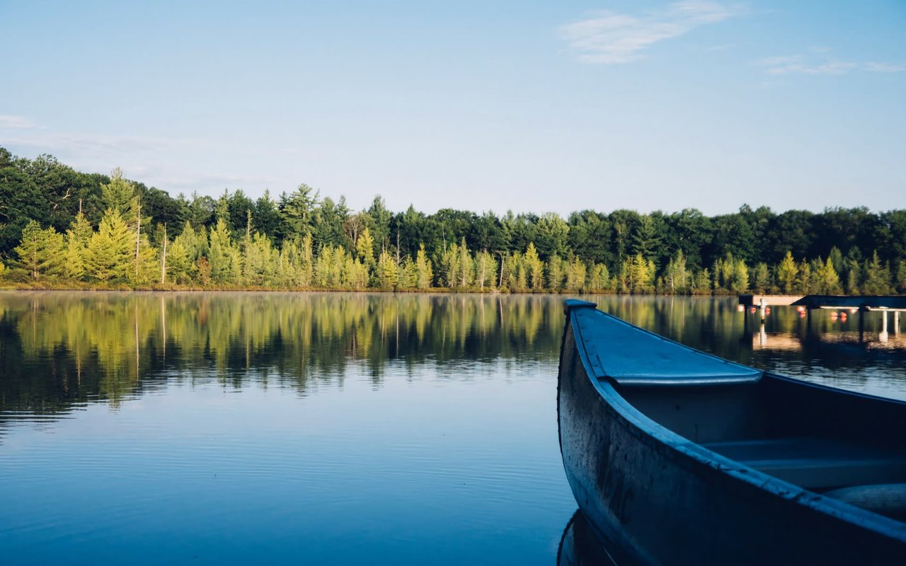  A blue canoe sits in the calm, reflective water of a lake, with its bow pointing towards the right side of the frame.