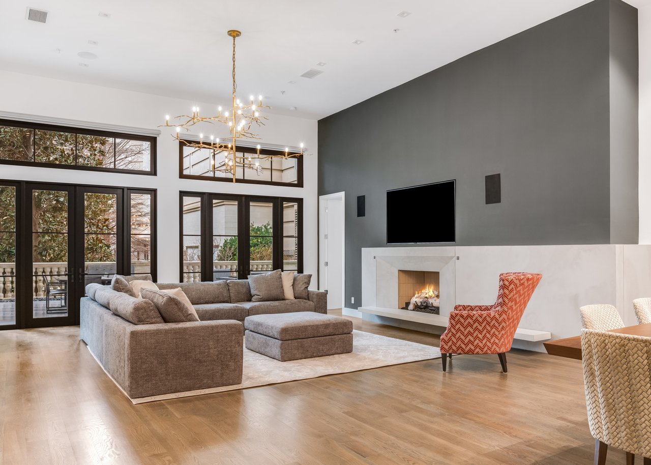 Spacious condo living room with a grey L-shaped couch, fireplace, TV, chandelier, and black framed doors leading to a patio.