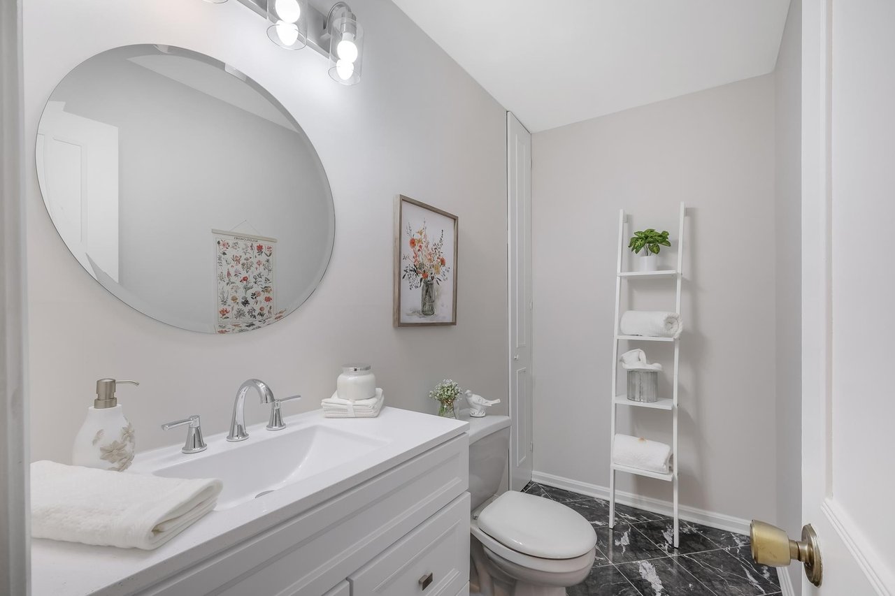 Bathroom with a white vanity, oversized round mirror, and black marble-look floor.