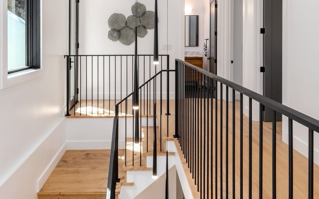 Modern oak staircase with black metal railings and pendant lights.
