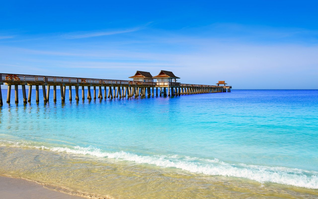  A long wooden pier stretches out over the calm, turquoise ocean under a clear blue sky.