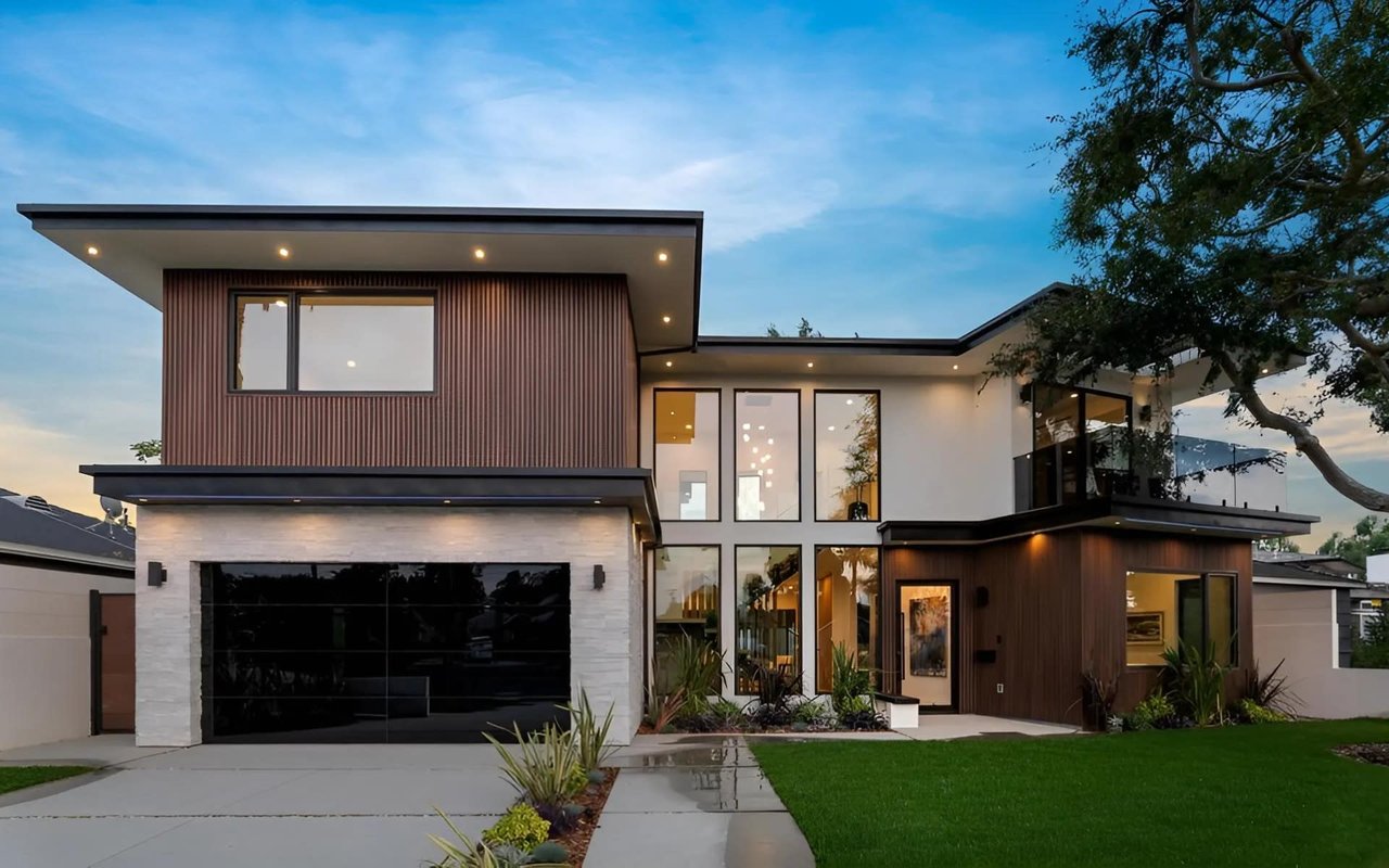 A modern 2-story house with a flat roof, black garage, white facade, brown accents, large windows, green lawn, and trees.