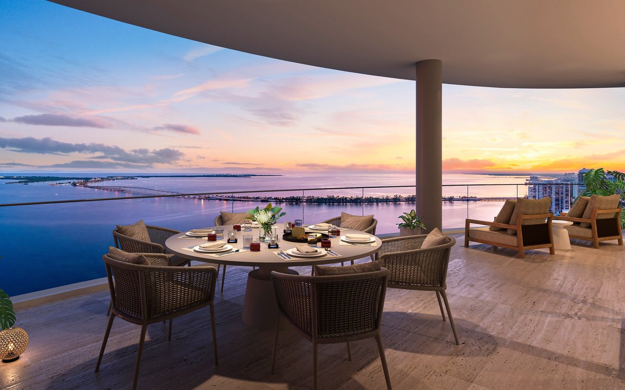 Furnished outdoor dining terrace overlooking the water at sunset, with a glass railing and Miami skyline.