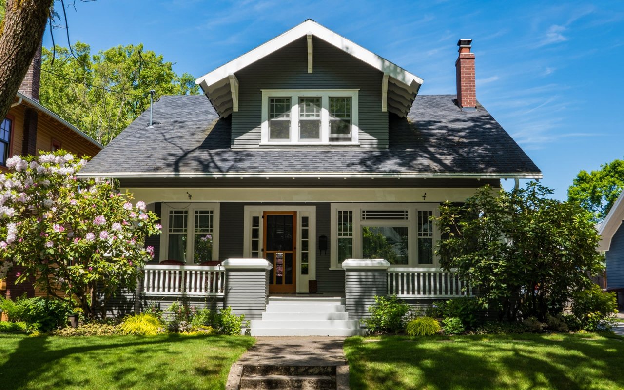 A gray house with a white front porch. The house has a dormer window and a screened front door.