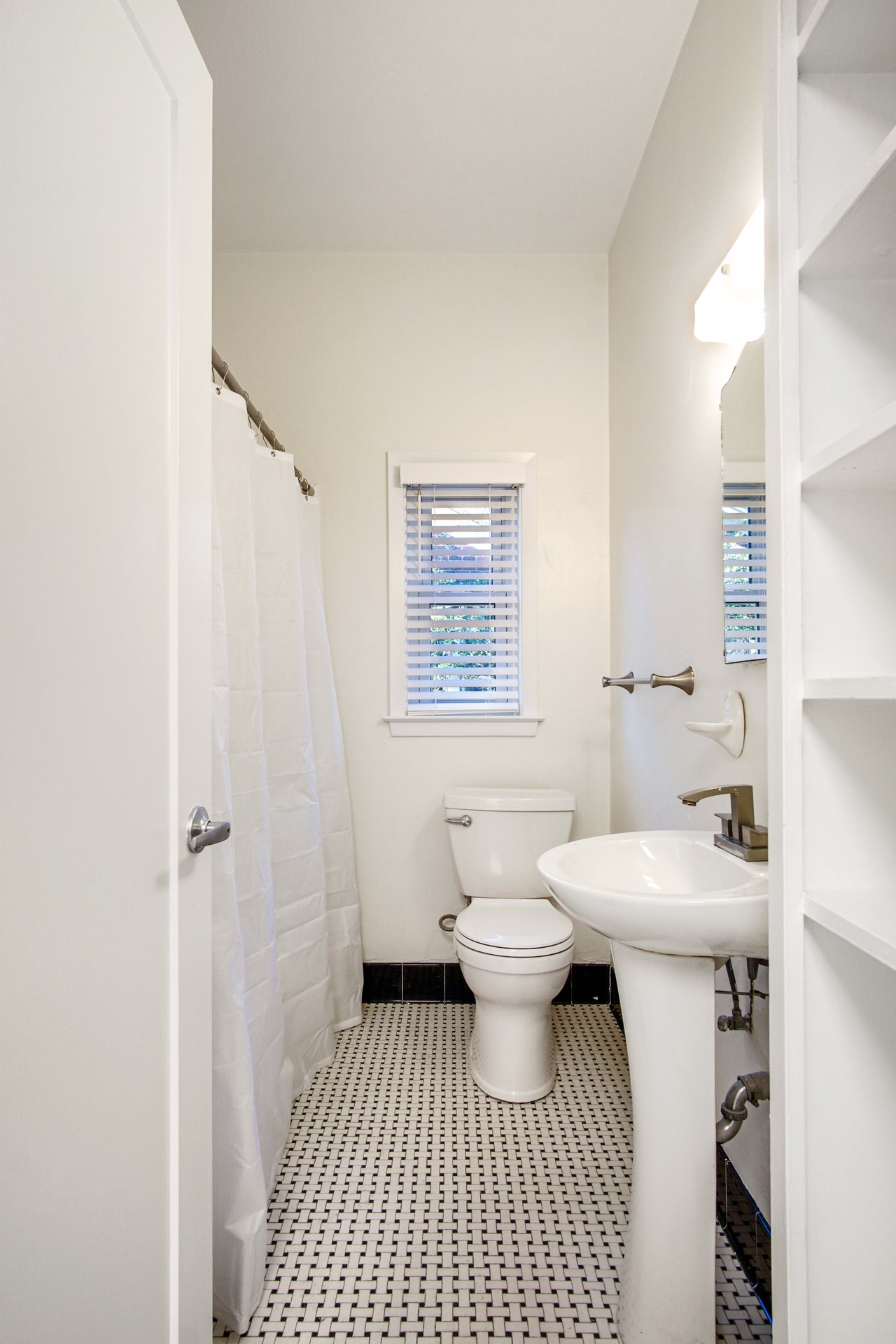A bathroom featuring a toilet, sink, and shower/tub combo. The room has white fixtures and a small window.