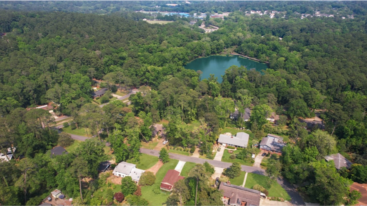  An aerial view of the San Luis community, highlighting houses, streets, and a central water feature. The area appears to be surrounded by dense greenery.