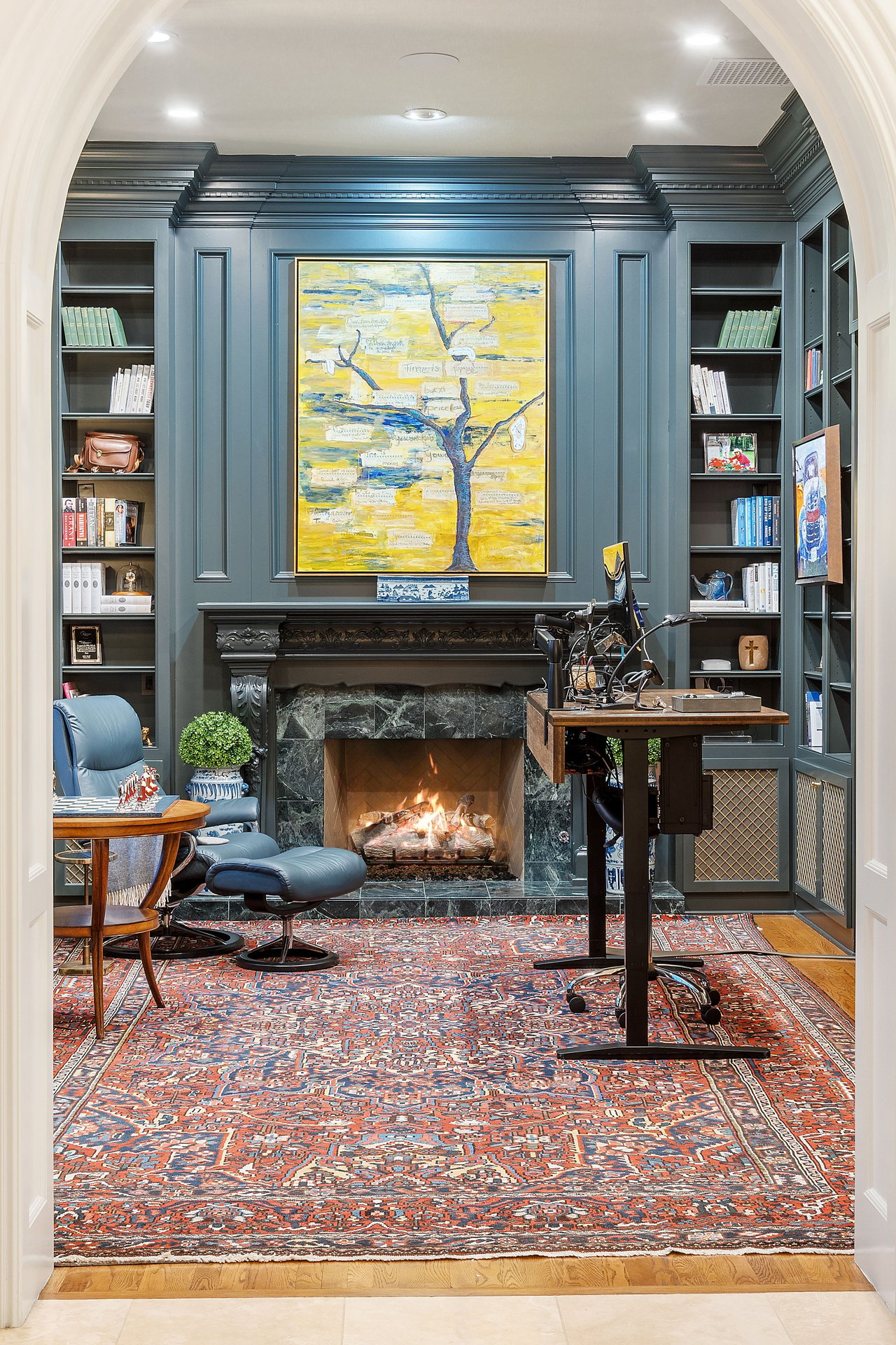 The library office  is adorned with tasteful finishes and decor. The room features rows of  built-in bookshelves, a cozy fireplace, and plenty of natural light. This handsome library office combines classic sophistication with contemporary functionality, creating a harmonious space for work, creativity, and personal expression.