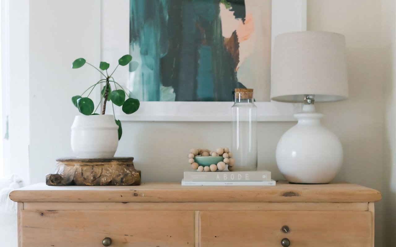 A wooden dresser with a white lamp, a green succulent in a white pot, and a book on top.