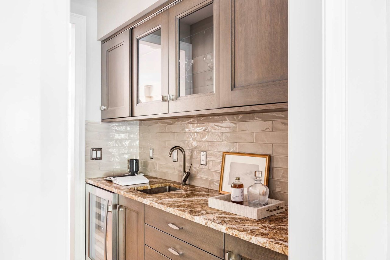 Built-in bar area with marble countertop, glass cabinets, and glossy subway tile backsplash