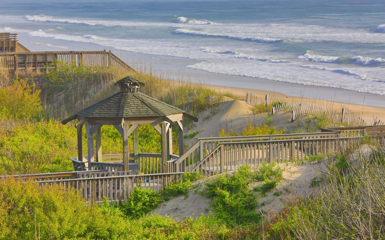 Octagonal-shaped wooden gazebo on an ocean-view seagrass dune with a shingled roof, railings, and a wooden walkway.