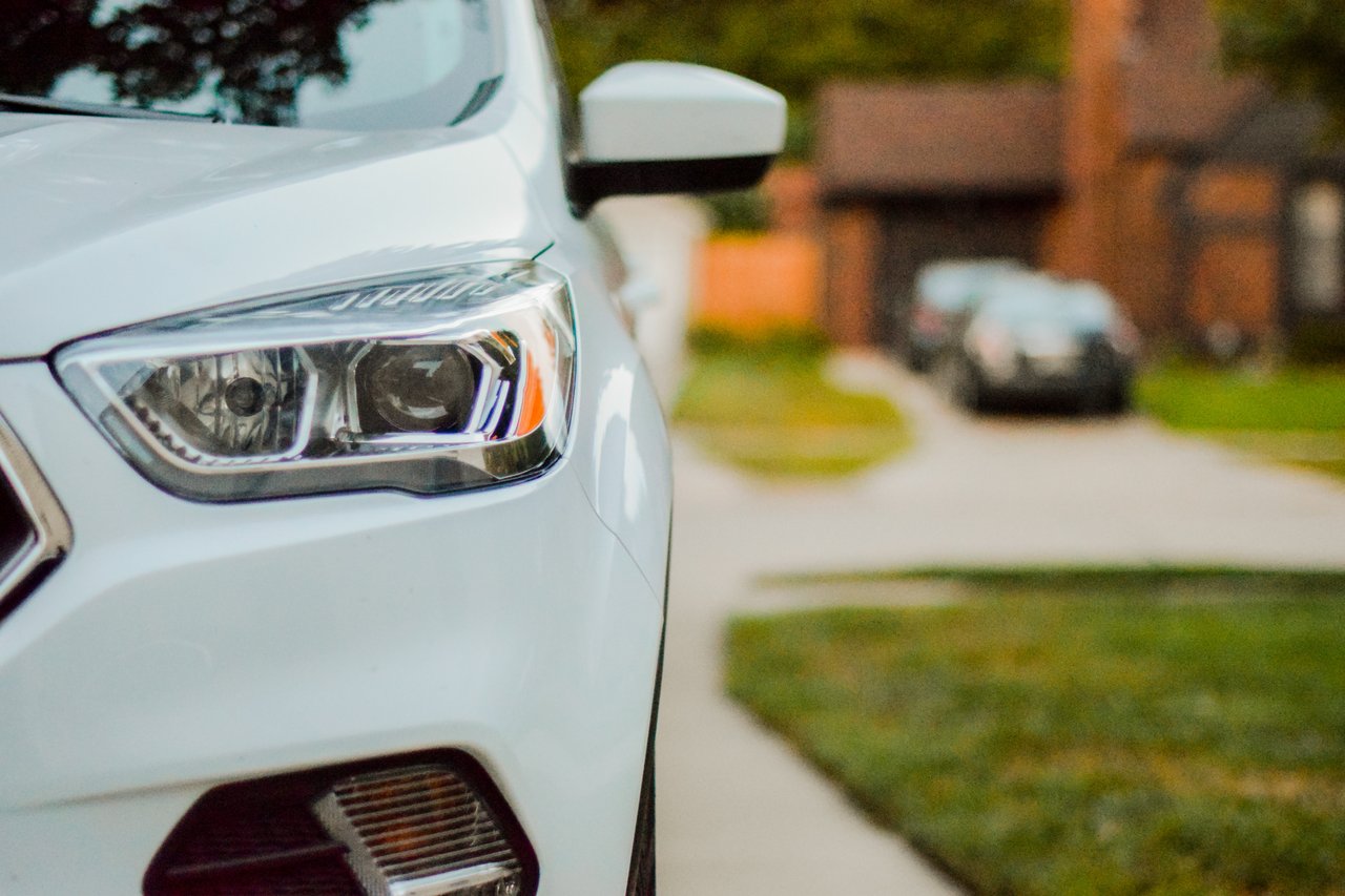 White car’s front headlight and bumper parked on a residential street.