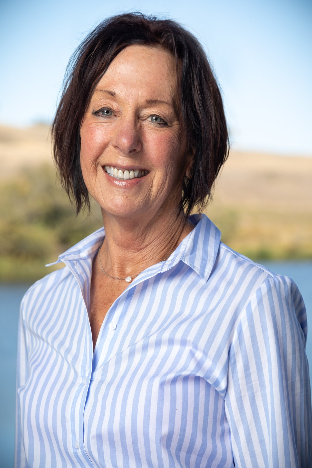 Mary Liebig smiling in a blue-and-white striped shirt outdoors.