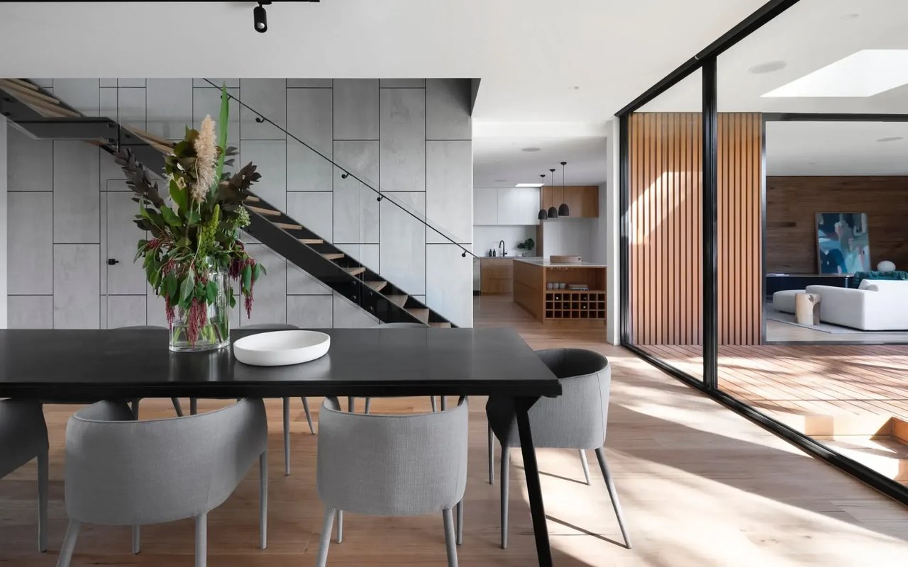  A dining room with a black table and gray chairs, a staircase, and large glass sliding doors leading to a patio.